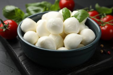 Lezzetli mozzarella peynir topları kasede, fesleğende, biberlikte ve domateslerde siyah masada, yakın plan.