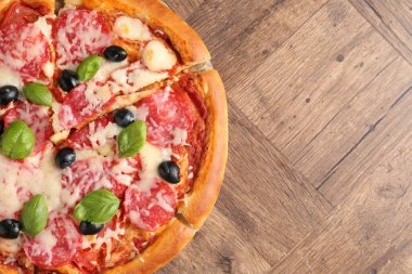 Tahta masada salamlı, peynirli, fesleğenli ve zeytinli lezzetli pizza. Metin için boşluk