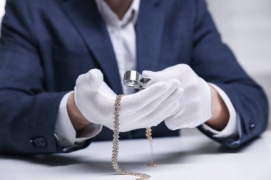 Beyaz masa içerisindeki lüks gerdanlığı değerlendiren eksper, yakın plan.