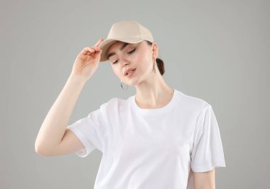 Gri arka planda şık beyzbol şapkalı güzel bir kadın.