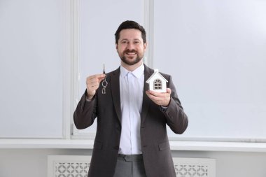 Emlakçının elinde anahtarlık ve ev modeli var.