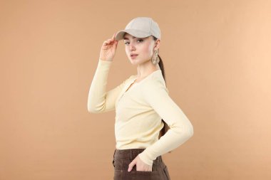 Bej arka planda şık bir beyzbol şapkası takmış güzel bir kadının portresi.