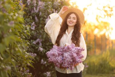 Gülümseyen kadın sabah çalıların yanında bir sepet leylak çiçeğiyle