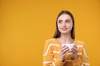 Sarı arka planda bir fincan kahveyle gülümseyen kadın. Metin için boşluk