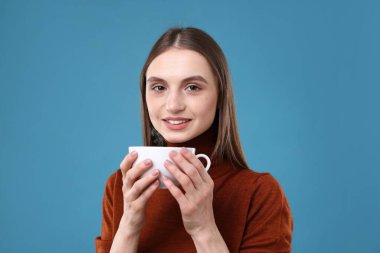 Açık mavi arka planda bir fincan kahveyle gülümseyen kadın.