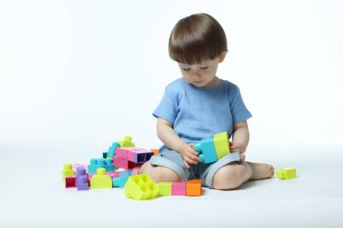 Beyaz arka planda tuğlalarla oynayan sevimli küçük çocuk.