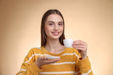 Bej renkli arka planda bir fincan kahveyle gülümseyen kadın