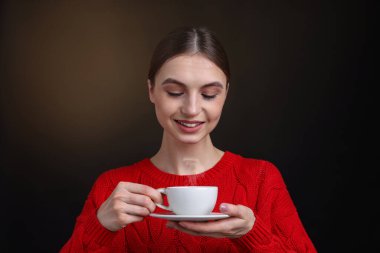 Kahverengi arka planda bir fincan kahveyle gülümseyen kadın.