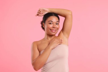 Pembe arka planda epilasyon işleminden sonra kılsız koltuk altını gösteren bir kadın.