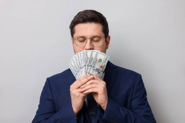 Açgözlü bankacı, gri arka planda dolar banknotlarını kokluyor.