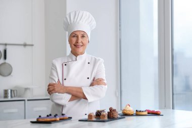 Gülümseyen pasta şefi mutfaktaki tatlılarla masada.