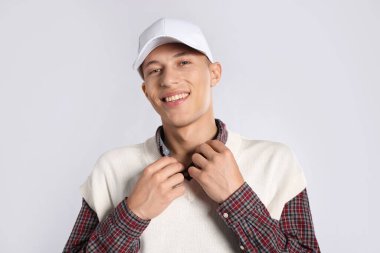 Açık gri arka planda şık bir beyzbol şapkası takan genç adam.