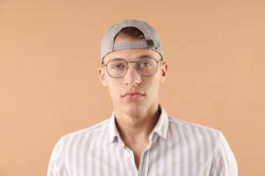 Beyzbol şapkalı genç adam bej arka planda.