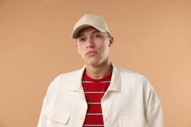 Beyzbol şapkalı genç adam bej arka planda.