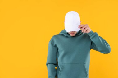 Sarı arka planda şık beyaz beysbol şapkası giyen genç adam, mesaj için yer var.