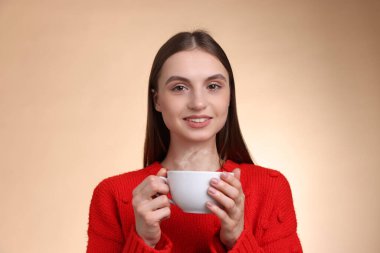 Bej renkli arka planda bir fincan kahveyle gülümseyen kadın