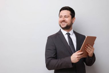 Açık gri arka planda tableti olan gülümseyen bir işadamı. Metin için boşluk