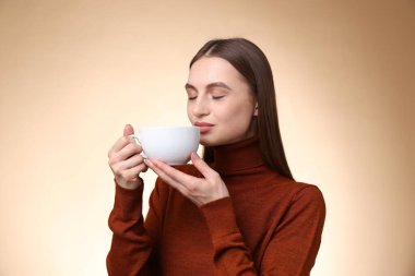 Bej renkli arka planda fincandan kahve içen kadın