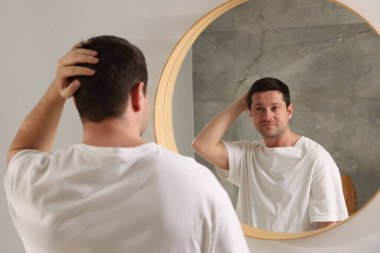 Yakışıklı adam aynada kendine bakıyor.