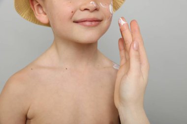 Anne açık gri arka planda oğlunun cildine güneş kremi sürüyor. Yakın plan.