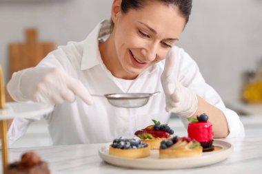 Şekerci masadaki tartın üzerine pudra şekeri serpiyor.
