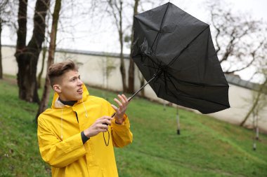 Kırık şemsiyeli bir adam açık havada yağmur altında rüzgarla savaşıyor.