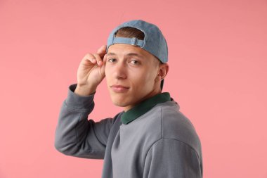 Pembe arka planda şık bir beyzbol şapkası takan genç adam.