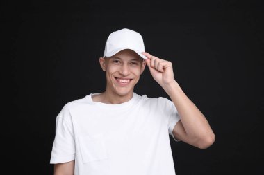 Siyah arka planda şık beyaz beysbol şapkası giyen genç bir adam.