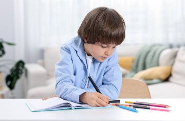 Evde, masada ödev yapan sevimli küçük çocuk.