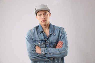 Açık gri arka planda şık bir beyzbol şapkası takan genç adam.