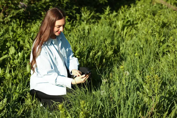 Güneşli bir günde akıllı telefondan bitki tanıma uygulaması kullanan gülümseyen kadın.