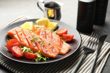 Lezzetli ızgara somon, marul, domates ve limonla servis edilir.