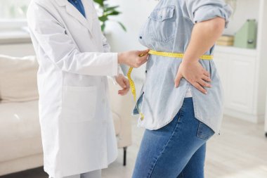 Kilo kaybı. Klinikte kilolu kadının belini bantla ölçen beslenme uzmanı.
