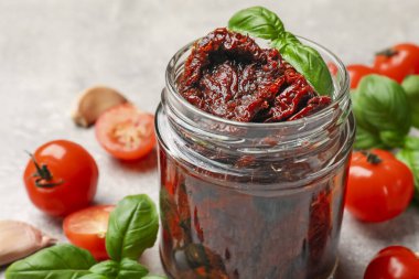 Lezzetli güneşte kurutulmuş domatesler, taze sebzeler, fesleğen ve sarımsak açık gri masada, yakın plan.