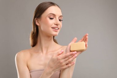 Gri arka planda sabun çubuğuyla gülümseyen kadın.