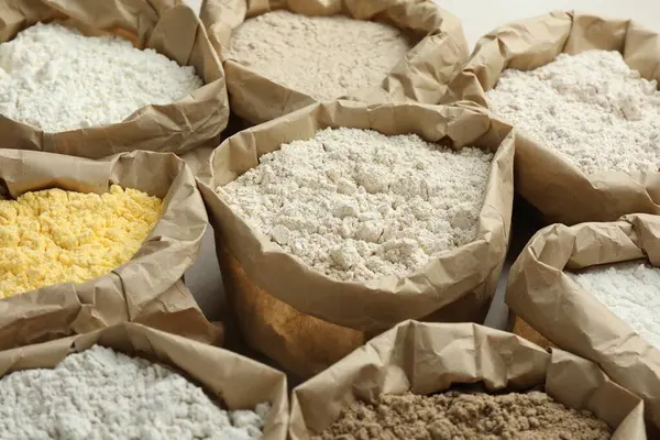 Beyaz masadaki kağıt torbalarda farklı türde un, yakın plan.