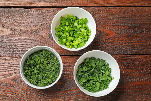 Tahta masadaki kaselerde farklı taze otlar.