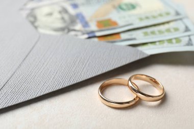 İki altın alyans, bir dolarlık banknotlar ve beyaz masanın üzerindeki zarf, yakın plan.