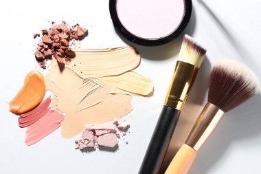 Beyaz arka planda farklı kozmetik ürünler ve makyaj fırçaları, düz yatış