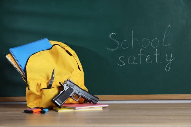 Sırt çantasında silah, bıçak ve kırtasiye malzemeleri var. Tahtanın yanındaki tahta masada. Okul güvenliği