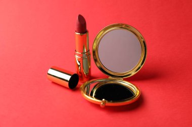 Kırmızı arkaplanda cep aynası ve ruj, yakın plan.
