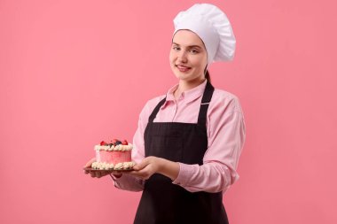 Şekerci pembe arka planda lezzetli bir pasta tutuyor.