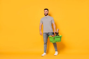 Turuncu arka planda ürünlerle dolu alışveriş sepeti olan bir adam.