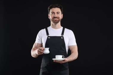 Siyah arka planda kahve yapan gülümseyen baristanın portresi.