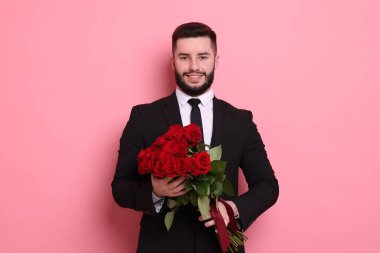 Pembe arka planda kırmızı güller açan mutlu bir adam.