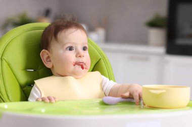 Evdeki beslenme sandalyesinde yemek yiyen şirin bir bebek.