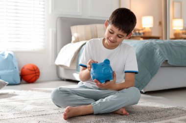 Çocuk evdeki domuz kumbarasına cep harçlığı koyuyor.