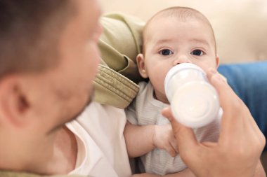 Babası evdeki kanepede bebeğini biberonla besliyor.