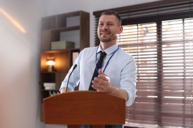 İçerideki kürsüde mikrofonla halka açık konuşma yapan adam.