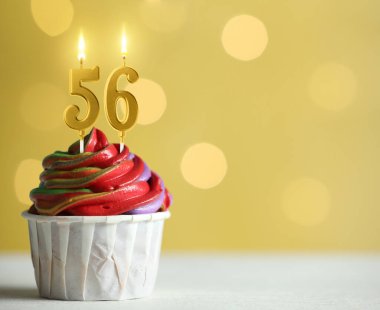 Sarı zemin üzerinde yanan mumlar, bulanık ışıklar ve yazı için yer olan enfes bir kek. 56. yaş günü veya diğer özel günler